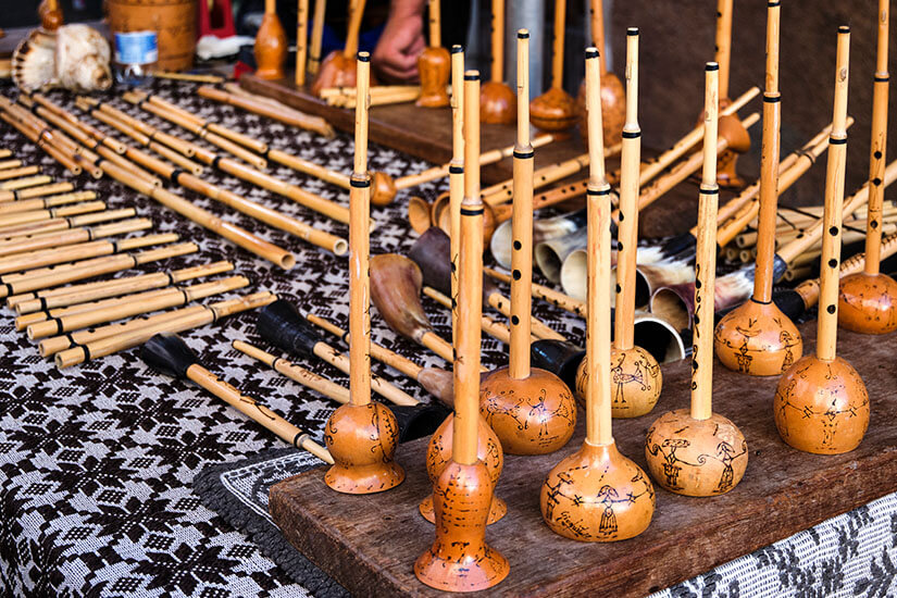 Auf einem Marktstand liegen zahlreiche traditionelle Blasinstrumente aus Holz und Rohr. Einige besitzen kugelförmige Resonanzkörper und lange, dünne Röhren mit kleinen Verzierungen. Sardinien Musikinstrument
