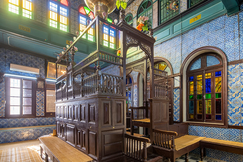 Das prachtvolle Innere der El Ghriba Synagoge mit blau verzierten Kachelwänden, kunstvollen Holzstrukturen und buntem Lichteinfall durch Buntglasfenster. Houmt Souk Tunesien El Ghriba Synagoge
