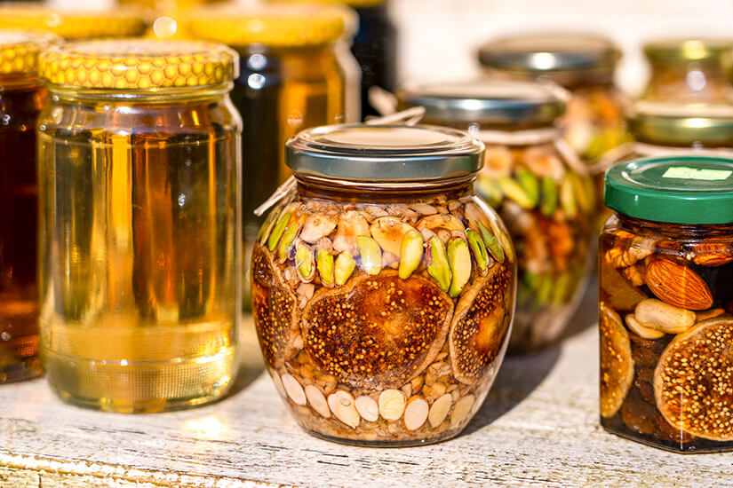 Mehrere Einweggläser sind mit Honig sowie verschiedenen Nüssen und Trockenfrüchten wie Feigen, Pistazien und Mandeln gefüllt und dekorativ arrangiert. Montenegro Souvenirs Honig