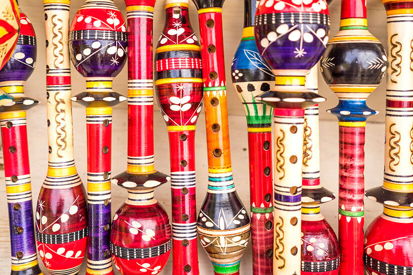 Eine Vielzahl bunt bemalter Holzflöten mit aufwendigen Mustern in kräftigen Farben wie Rot, Blau, Lila und Gelb sind dicht nebeneinander arrangiert. Montenegro Souvenirs Floete