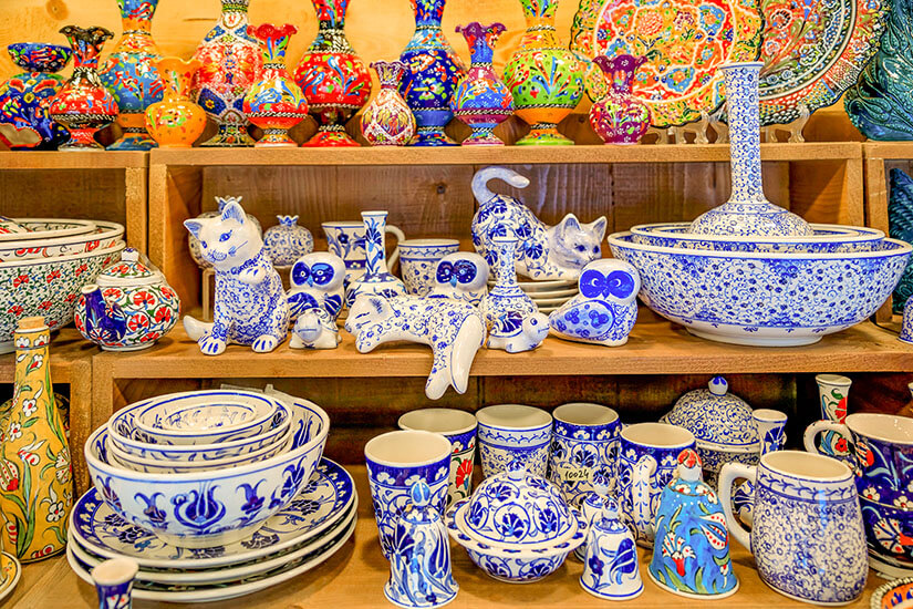 Holzregale sind reich bestückt mit traditioneller Keramik in charakteristischem Blau-Weiß mit floralen Mustern sowie bunten Vasen, darunter Schalen, Tassen und dekorative Tierfiguren wie Katzen und Eulen. Montenegro Souvenirs Keramik