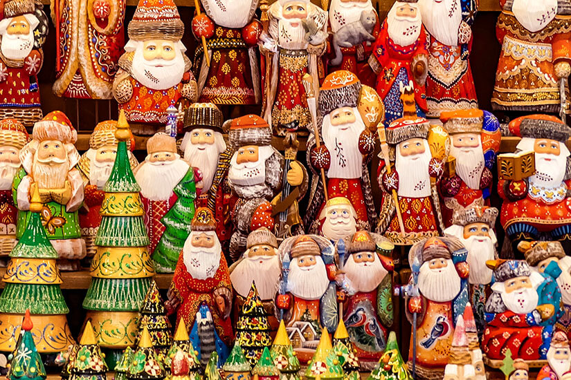 Eine dichte Sammlung handgeschnitzter und bunt bemalter Figuren in traditionellen roten Gewändern, ergänzt durch dekorative Weihnachtsbäume aus Holz, füllt das gesamte Bild. Weihnachtsschmuck Kotor