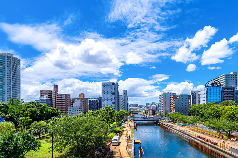 Ein breiter Kanal zieht sich durch das moderne Stadtbild Sendais, flankiert von Hochhäusern und sattem Grün. Weiße Wolken ziehen über eine lebhafte, aber nicht hektische Großstadt. Sendai zeigt sich hier als modernes urbanes Zentrum der Region Miyagi. Sendai Japan Sendaihori.