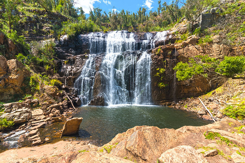 Ein breiter, mehrstufiger Wasserfall stürzt über rotbraune Felsen in ein natürliches Becken – ein typisches Bild der Naturparks in Australiens Grampians-Region. Die umliegende Buschvegetation und die markanten Gesteinsschichten machen diesen Ort zu einem beliebten Wanderziel. MacKenzie Falls gehört zu den besten Naturerlebnissen in Australiens Nationalparks. Nationalparks Australien Grampians National Park