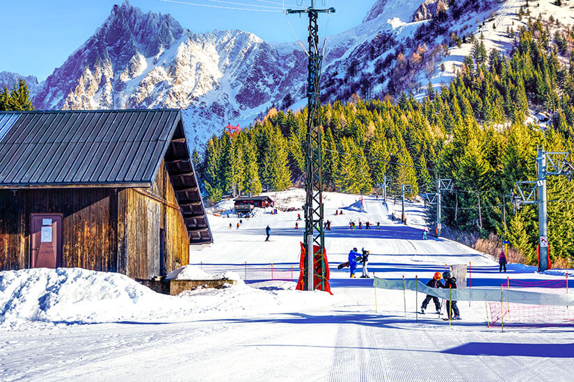 Skifahrer am Ende einer Abfahrt im Schnee. Grüne Wälder und eine Holzhütte umgeben das Bild. Engelberg Schweiz Ski