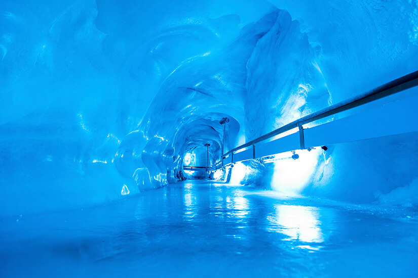 Ein Gang mit Geländer führt durch eine blau-weiß schimmernde Eishöhle. Engelberg Schweiz Hoehle