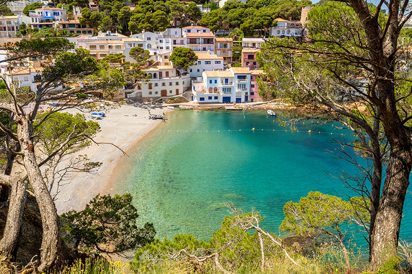 Eine grünblaue Bucht am Sandstrand, umgeben von weißen Häusern und Bäumen. Begur Spanien Sa Tuna