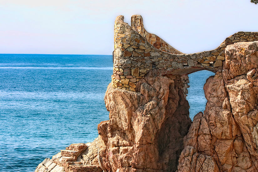 Eine bizarre Felsformationen aus rötlichem Stein ragt aus dem blauen Meer. Begur Spanien Wandern