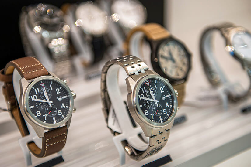 Mehrere Armbanduhren stehen in einer Auslage, teils mit Leder-, teils mit Metallarmband. Die Zifferblätter sind klar gestaltet und zeigen zusätzliche Funktionen wie kleine Chronographenanzeigen. Im Hintergrund sind weitere Modelle unscharf zu erkennen. Schweizer Uhren