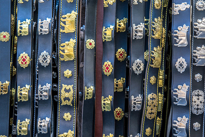Mehrere schwarze Ledergürtel hängen dicht nebeneinander und sind reich verziert. Metallapplikationen in Gold- und Silbertönen zeigen Motive wie Kühe und ornamentale Muster. Appenzell Gürtel