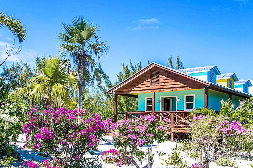 Die bunten Holzhäuser im Hintergrund und die üppige tropische Vegetation vervollständigen das Bild eines idyllischen Inselresorts. Luxus Reiseziele Bahamas