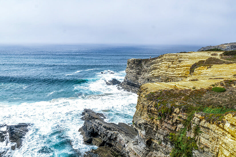 Das Meer rauscht in Wellen gegen hohe Klippen. Fischerweg Portugal Alentejo