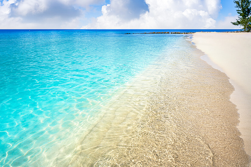 Kristallklares, türkisfarbenes Wasser spült sanft an einen hellen, feinsandigen Strand unter einem leicht bewölkten blauen Himmel am Playa Palancar. Cozumel Mexiko Playa Palancar