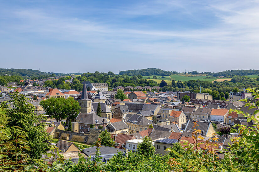 Die Stadt Valkenburg mit roten und braunen Dächern sowie dem Kirchturm ist zu sehen. Grün blühende Landschaft umgibt die Szene. Valkenburg Niederlande Wetter
