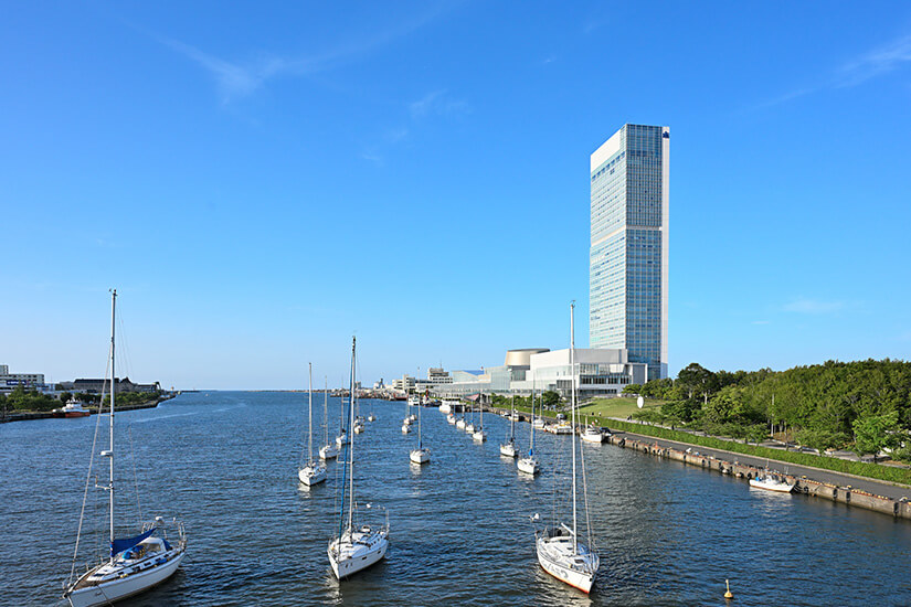 Blick über den Shinano-Fluss mit zahlreichen ankernden Segelbooten auf das markante Hochhaus der Toki Messe in Niigata unter strahlend blauem Himmel. Niigata Japan Toki Messe