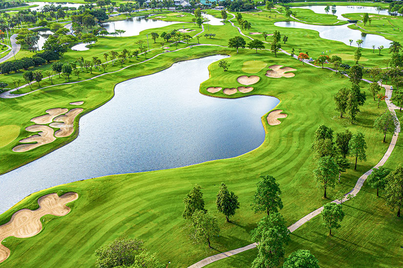 Eine weitläufige Anlage mit geschwungenen Wasserflächen, strategisch platzierten Sandbunkern und tropischem Baumbestand erstreckt sich unter einem leuchtend grünen Teppich. Die Architektur des Platzes nutzt Wasser als zentrales Gestaltungselement und fordert präzises Spiel. Südostasiens Golfszene zeigt sich hier von ihrer besten Seite. Golfdestinationen weltweit Thailand
