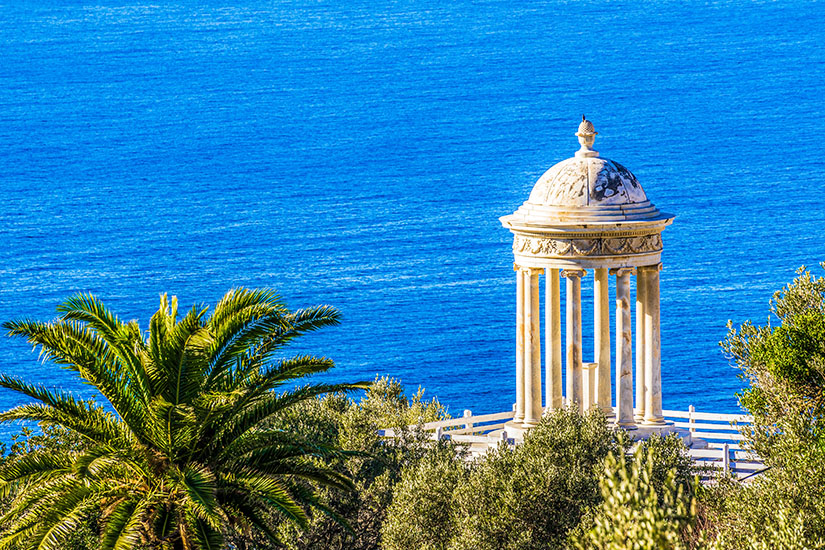 Ein weißer Pavillon an der Küste Mallorcas ist zu sehen. Im Hintergrund glitzert das blaue Meer. Deia Spanien Aussichtspunkt