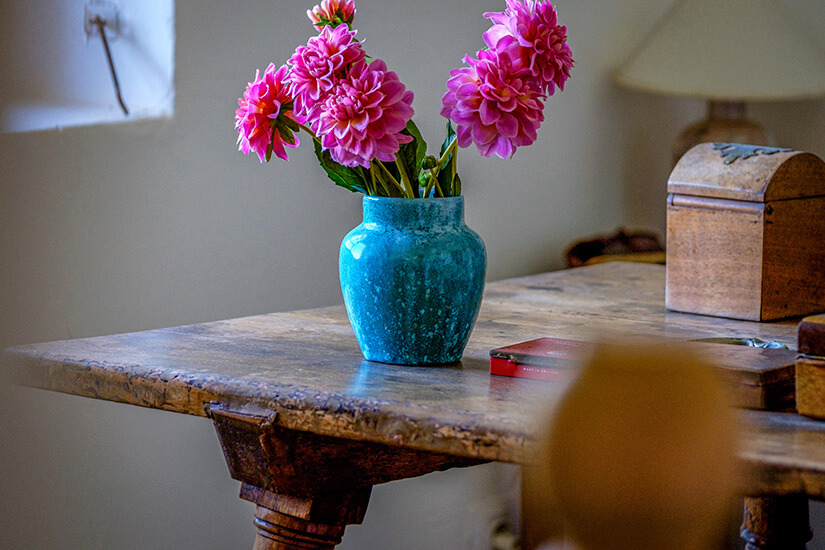 Eine blaue Vase mit rosaroten Blumen steht auf einem Holztisch. Deia Spanien Robert Graves