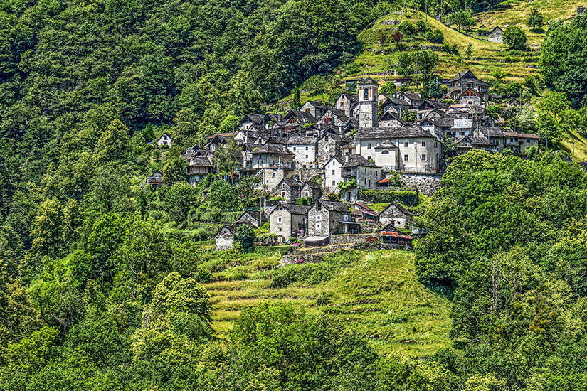 Corippo ist das kleinste Dorf der Schweiz und eines der schönsten Orte im Verzascatal. Die charakteristischen Steinhäuser schmiegen sich malerisch an den grünen Berghang im Tessin und wirken wie aus der Zeit gefallen. Das autofreie Dorf gehört zu den bedeutendsten Sehenswürdigkeiten der Valle Verzasca und steht unter Denkmalschutz. Verzascatal Schweiz Corippo