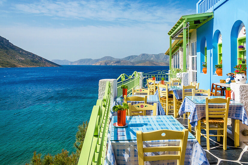 Dieses Bild verkörpert die Quintessenz des griechischen Insellebens – entspanntes Speisen mit unverbautem Meeresblick in typisch mediterraner Farbenpracht. Kos oder Korfu Restaurant