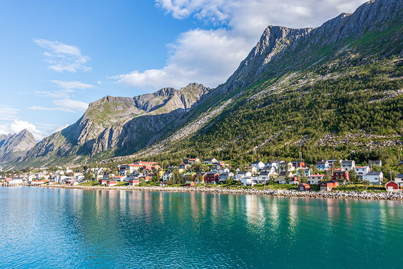 Das malerische Fischerdorf Gryllefjord liegt wie hingetupft am Fuße mächtiger Berge an einem smaragdgrünen Fjord. Die bunten Holzhäuser spiegeln sich im ruhigen Wasser und erzählen von traditionellem norwegischem Küstenleben. Gryllefjord ist einer der charmantesten Orte auf der Insel Senja Norwegen und ein beliebter Ausgangspunkt für Fährverbindungen. Senja Norwegen Gryllefjord