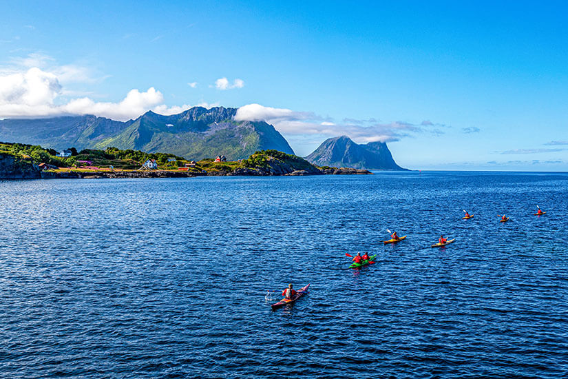 Kajaks gleiten über das tiefblaue Meer vor der Küste von Senja, im Hintergrund ragen grüne Berge und kleine Inseln empor. Die Szene strahlt pure Freiheit und Abenteuer aus – Seekajakfahren gehört zu den beliebtesten Senja Aktivitäten. Von der Wasserperspektive aus zeigt sich die Insel Senja Norwegen von ihrer allerschönsten Seite. Senja Norwegen Kayak