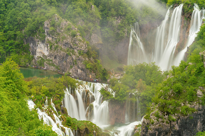 Weiße Wasserfälle stürzen über Felsen in einer Umgebung mit viel Grün. Ein blau-grüner See ist außerdem zu sehen. Wasserfaelle Kroatien Veliki