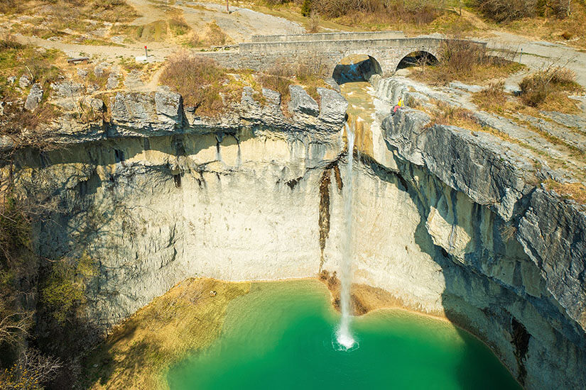 Ein Wasserfall ergießt sich über eine Felswand in eine Schlucht. Das Wasser darunter leuchtet grün und türkis. Wasserfaelle Kroatien Sopot