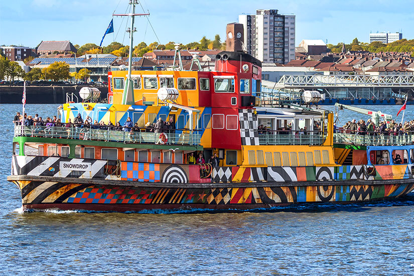 Die auffällig bunt mit geometrischen Mustern und Pop-Art-Elementen bemalte Fähre „Snowdrop“ transportiert zahlreiche Passagiere über den glitzernden Mersey-Fluss vor der Skyline von Liverpool. Liverpool England Faehre
