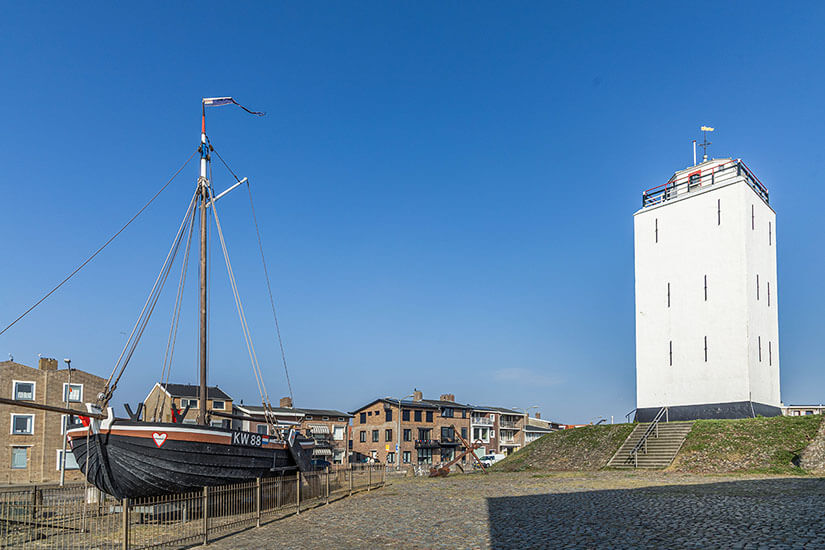 Der Leuchtturm von Katwijk, auch Vuurbaak genannt, ist das unverkennbare Wahrzeichen der Stadt und steht direkt an der Promenade hinter dem Deich. Mit seinem weiß getünchten, markant quadratischen Turm diente er jahrhundertelang den Fischern als wichtige Orientierung. Neben dem Leuchtturm erinnert ein historisches Fischerboot an die maritime Vergangenheit von Katwijk aan Zee. Katwijk aan Zee Niederlande Leuchtturm
