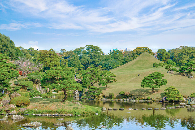 Der Suizenji-Garten mit seinem charakteristischen Miniatur-Fuji-Hügel präsentiert sich als perfektes Beispiel japanischer Gartenkunst, umrahmt von kunstvoll geschnittenen Kiefern und einem klaren Teich. Die symbolische Landschaft bildet die 53 Stationen der historischen Tokaido-Straße im Kleinformat nach. Diese grüne Oase mitten in Kumamoto City lädt zum Verweilen ein und bietet eine wohltuende Pause vom städtischen Trubel. Kumamoto Japan Suizenji