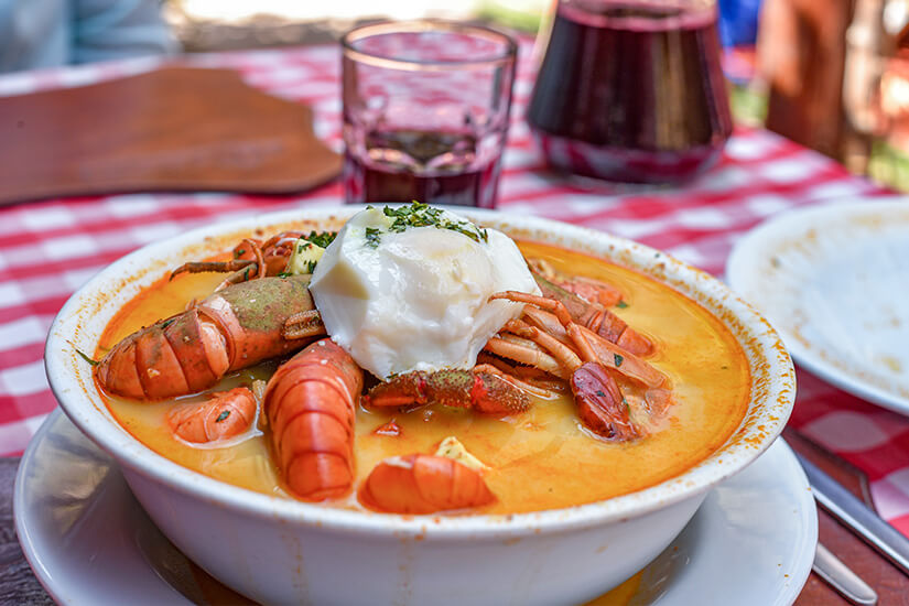 Chupe de Camarones mit ganzen Flussgarnelen in einem cremig-goldenen Fond, gekrönt von einem pochierten Ei wird auf einem rot-weiß karierten Tischtuch serviert. Peruanisches Essen Garnelen Eintopf