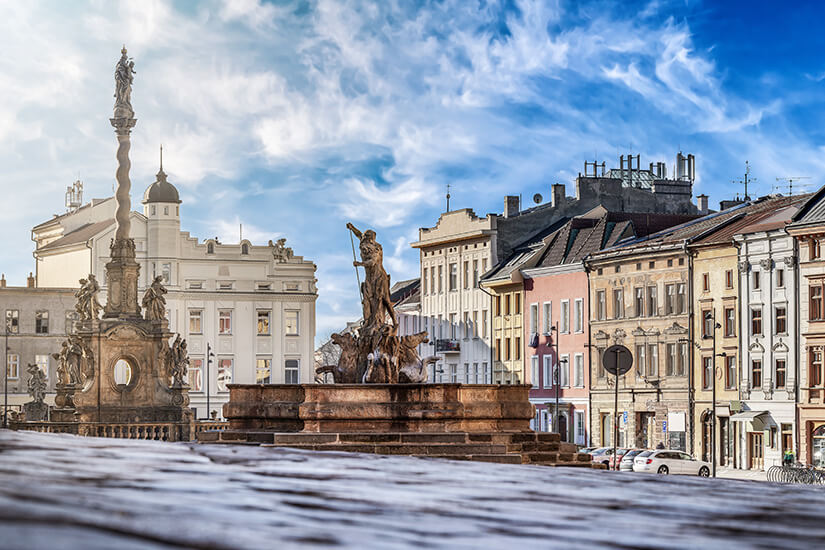 Der Caesarbrunnen ist einer der sieben barocken Brunnen in der Altstadt und zeigt den römischen Kaiser hoch zu Ross. Im Hintergrund ragt die Mariensäule zwischen prächtigen Bürgerhäusern empor. Die Szene fängt das einzigartige Flair der Olmütz Altstadt ein. Olomouc Tschechien Brunnen