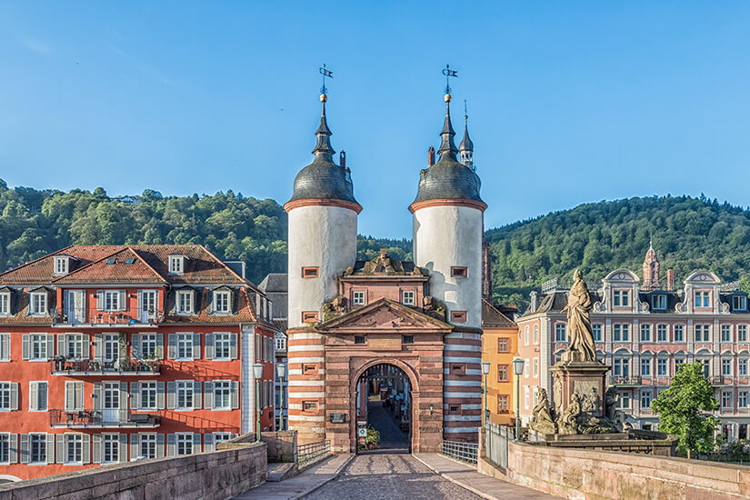 Ein Tor mit zwei weißen Türmen sitzt am Ende einer Brücke. Dahinter liegt die Altstadt von Heidelberg. Altstadt Deutschland Heidelberg