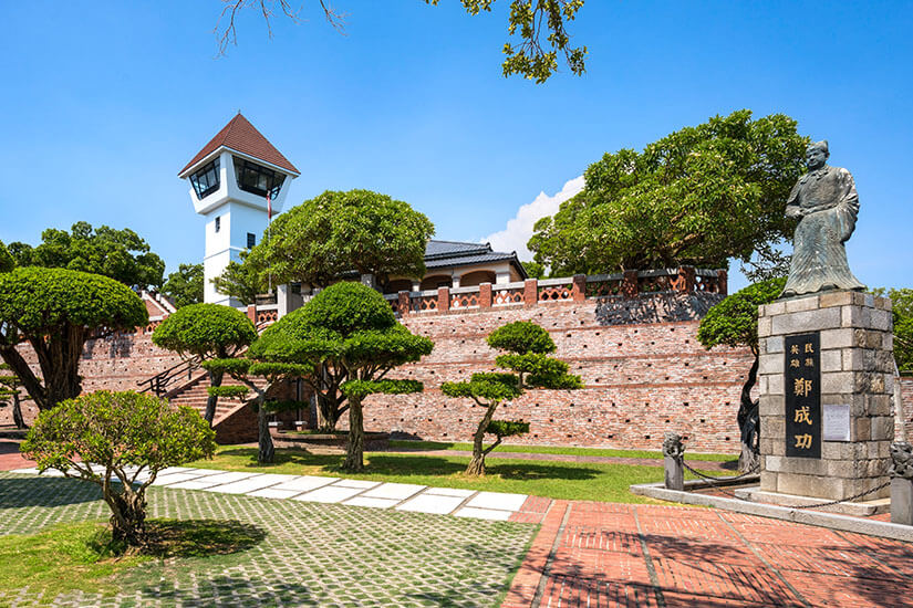 Das historische Anping Fort, einst von den Niederländern im 17. Jahrhundert als Fort Zeelandia errichtet, gehört zu den bedeutendsten kulturellen Stätten der Stadt. Die markante rote Backsteinmauer und der weiße Aussichtsturm sind umgeben von kunstvoll geformten Bonsai-Bäumen und gepflegten Gartenanlagen. Vor der Anlage steht die Statue des Nationalhelden Koxinga (Zheng Chenggong), der die niederländische Kolonialherrschaft beendete. Tainan Taiwan Anping