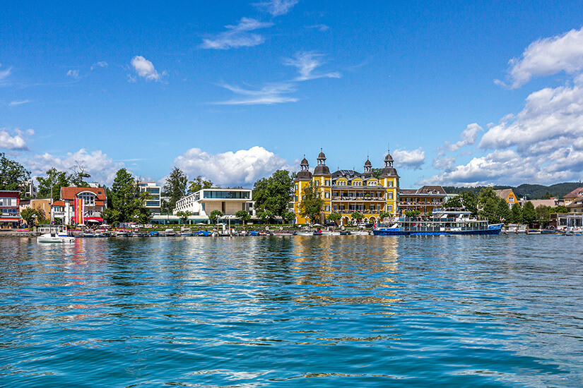 Ein Blick auf Velden am Ufer des Wörthersees. Das Schloss und einige Boote sind vom Wasser aus zu sehen. Velden Oesterreich Willkommen