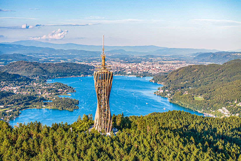 Der Turm Pyramidenkogel thront auf einem bewaldeten Gipfel und bietet eine grandiose Aussicht auf den blau leuchtenden Wörthersee. Velden Oesterreich Turm