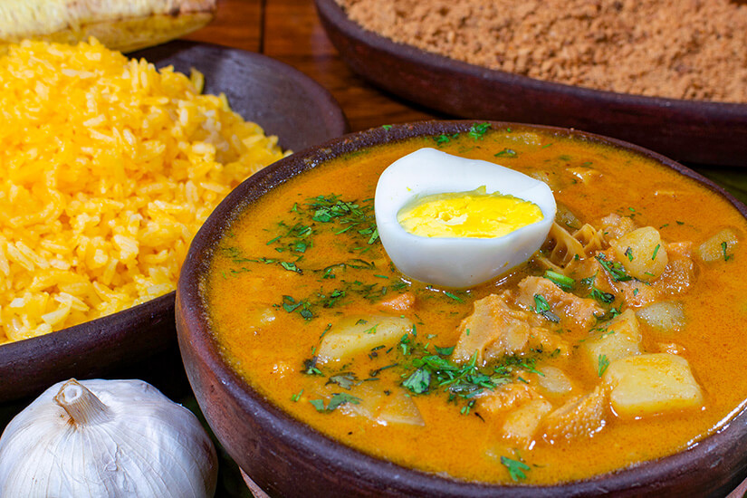 In einer dunklen Tonschale dampft ein herzhafter Eintopf aus Kutteln und Kartoffeln in cremiger Erdnusssoße, garniert mit einem halben hartgekochten Ei und frischem Koriander. Ecuador Essen Guatita