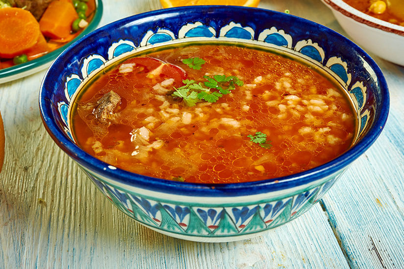 In einer kunstvoll blau-türkis bemalten Keramikschale dampft eine tomatenrote Suppe mit grünem Weizen, Lammfleisch und frischer Petersilie. Tunesisches Essen Frik
