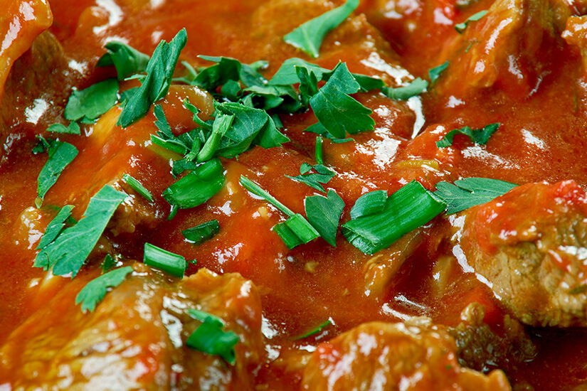 In einer dickflüssigen, kräftig roten Tomatensauce schmoren zarte Fleischstücke, garniert mit frisch gehackter Petersilie und Frühlingszwiebeln. Tunesisches Essen Kamounia