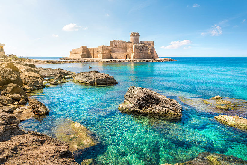 Die historische Festung Capo Rizzuto liegt direkt am türkisblauen Meer, umgeben von Felsen und kristallklarem Wasser. Die Szene wirkt ruhig, sonnig und ideal für Küsten- und Kultururlaub. Apulien oder Kalabrien Capo Rizzuto