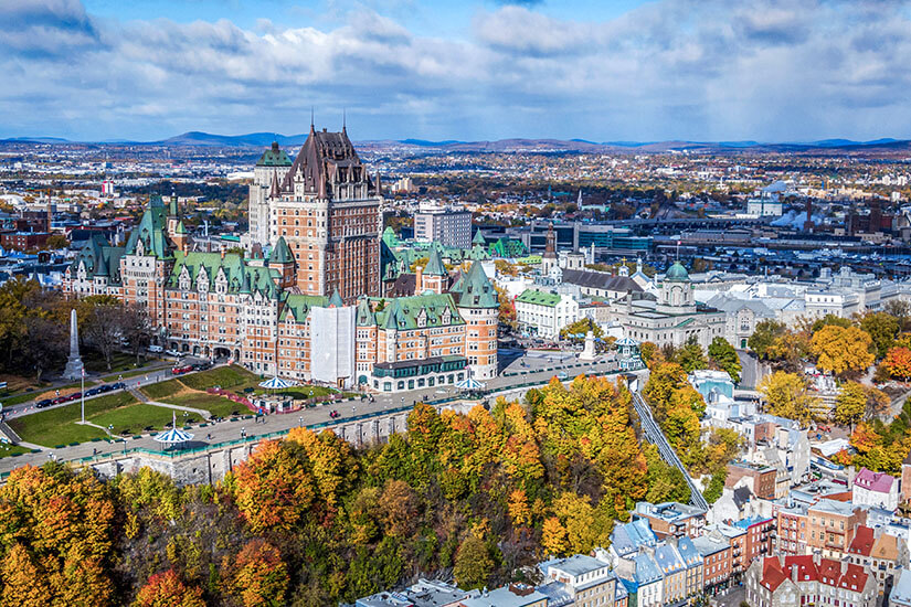 Ein rotes Gebäude mit grünem Dach thront über einer Stadt. Davor stehen einige Bäume mit herbstlich gefärbtem Laub. Kanada Staedte Quebec City