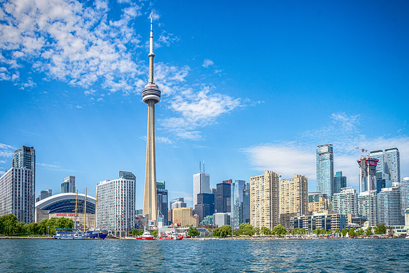 Skyline einer Stadt direkt am Wasser. Links ragt einer Fernsehturm in die Höhe. Kanada Staedte Toronto