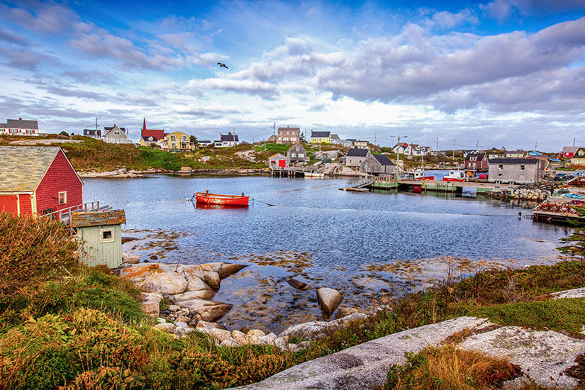 Ein kleines Fischerdorf mit bunten Häusern liegt auf Felsen am Wasser. Darauf ist ein kleines, rotes Boot zu sehen. Nova Scotia Halifax