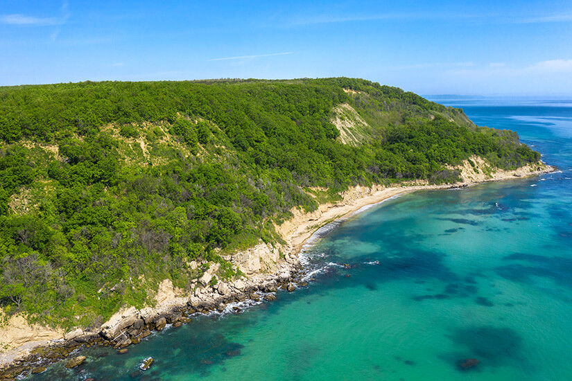 Ein sandiger Strand, umgeben von flachem Meerwasser und grüner Vegetation. Goldstrand Sonnenstrand Bulgarien Irakli Bech