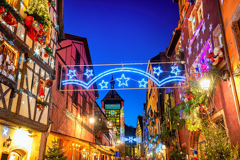 Blick bei Dämmerung in eine festlich beleuchtete Gasse von Riquewihr während der Weihnachtszeit. Riquewihr Frankreich Weihnachten