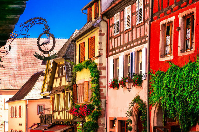 Eine charmante Reihe aus historischen Fachwerkhäusern in lebendigen Farben wie Rot, Rosa und Gelb säumt eine Gasse. Riquewihr Frankreich Fachwerk