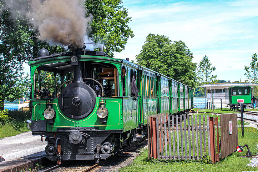 Die historische Chiemseebahn auf ihrer kurzen Strecke zwischen Bahnhof Prien und Schiffsanleger Stock. Die grüne Dampflok aus dem Jahr 1887 ist die älteste noch betriebene Dampfstraßenbahn der Welt. Sie verbindet auf nostalgische Weise Anreise und Schifffahrt zu den Chiemseeinseln. Chiemsee Deutschland Chiemseebahn