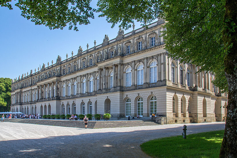 Die imposante Fassade von Schloss Herrenchiemsee, erbaut von König Ludwig II. nach dem Vorbild von Versailles. Das prunkvolle Bauwerk liegt auf der Herreninsel, der größten Insel im Chiemsee. Es zählt zu den meistbesuchten Sehenswürdigkeiten Bayerns. Chiemsee Deutschland Herrnchiemsee