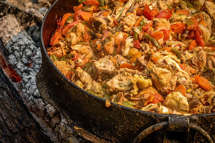In einem rußgeschwärzten gusseisernen Topf über offenem Holzfeuer schmort ein üppiges Hähnchengeschnetzeltes mit Tomaten, Karotten, Zwiebeln, grünen Bohnen und Paprika. Pollo Guisado Essen